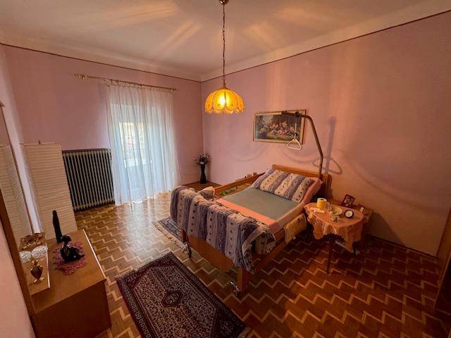 Schlafzimmer mit rosa Wänden, Parkettboden, einem Bett und einem großen Fenster für viel Tageslicht.