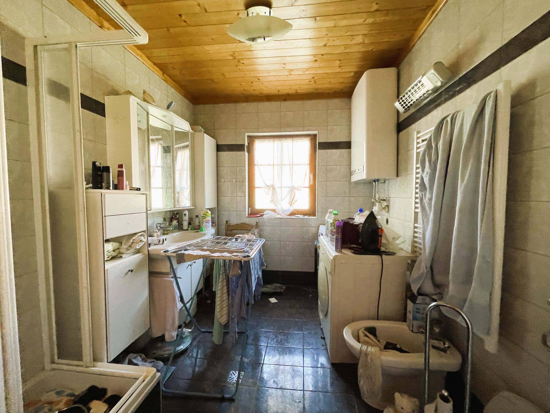 Funktionales Badezimmer mit Fliesen, Holzdecke, Dusche, WC und Waschmaschine.
