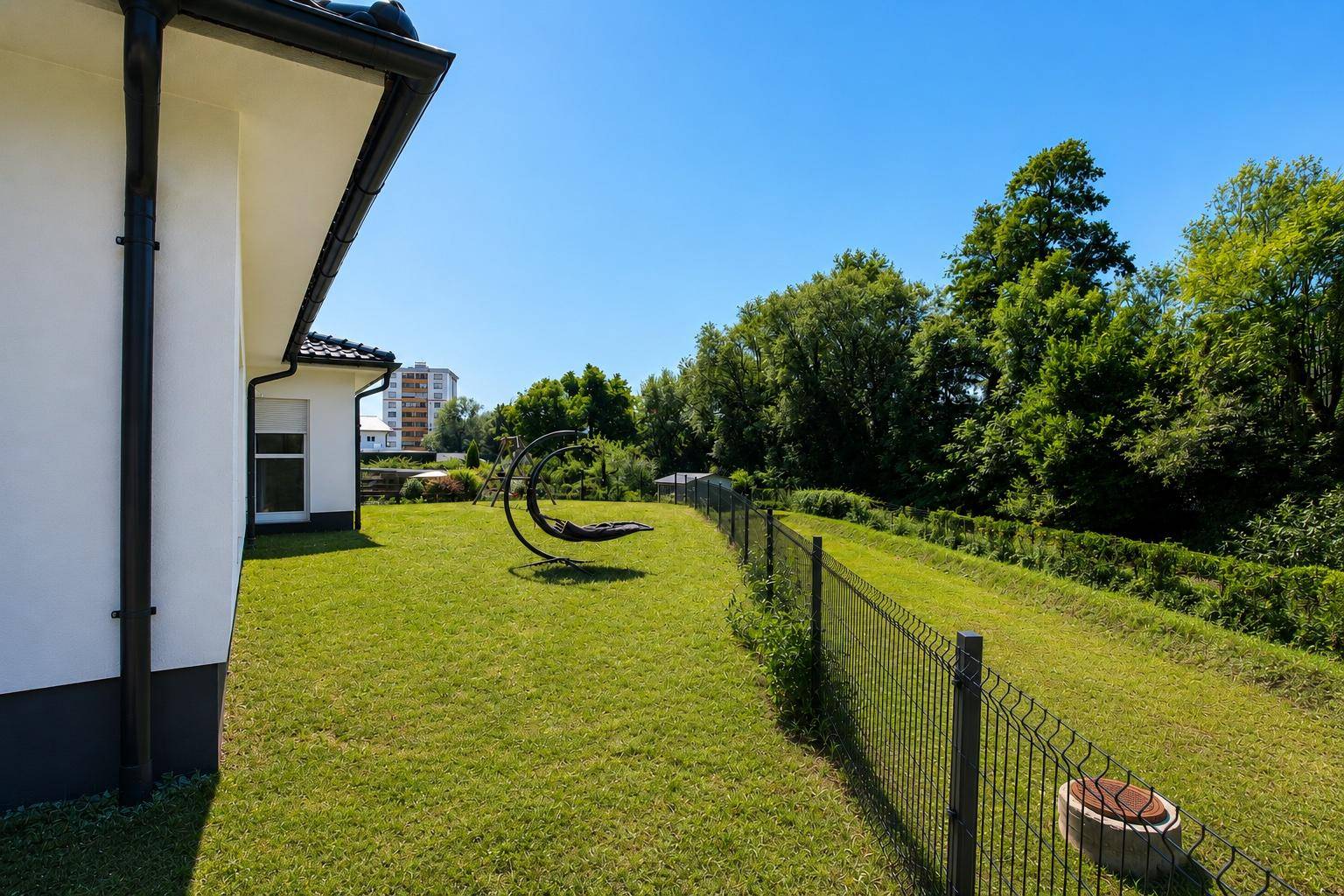 Seitliche Ansicht des Gartens mit Rasenfläche, Zaun und einer modernen Hängeliege.