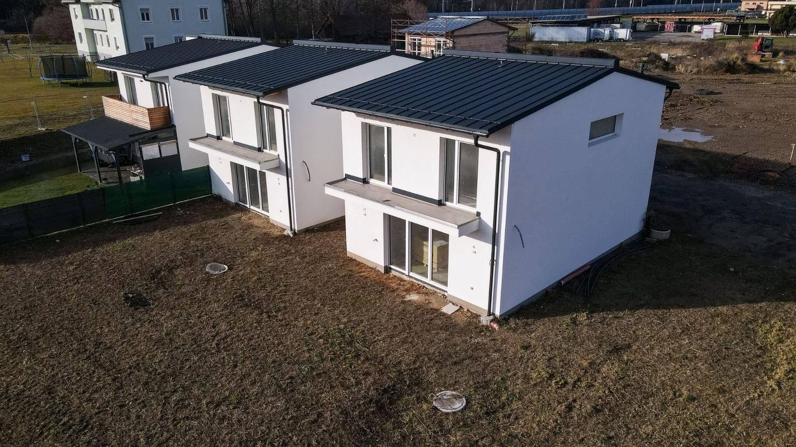Luftaufnahme von drei neuen Häusern mit dunklen Dächern und weißer Putzfassade.