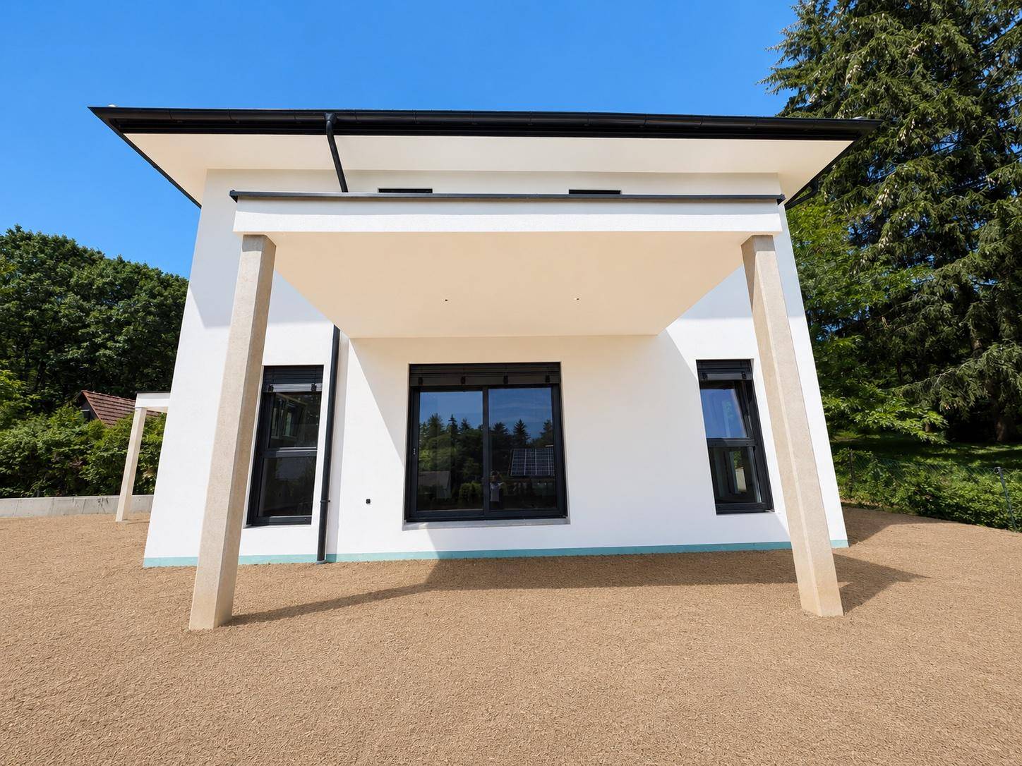 Vorderansicht des modernen Hauses mit überdachter Terrasse und großen Glasschiebetüren.