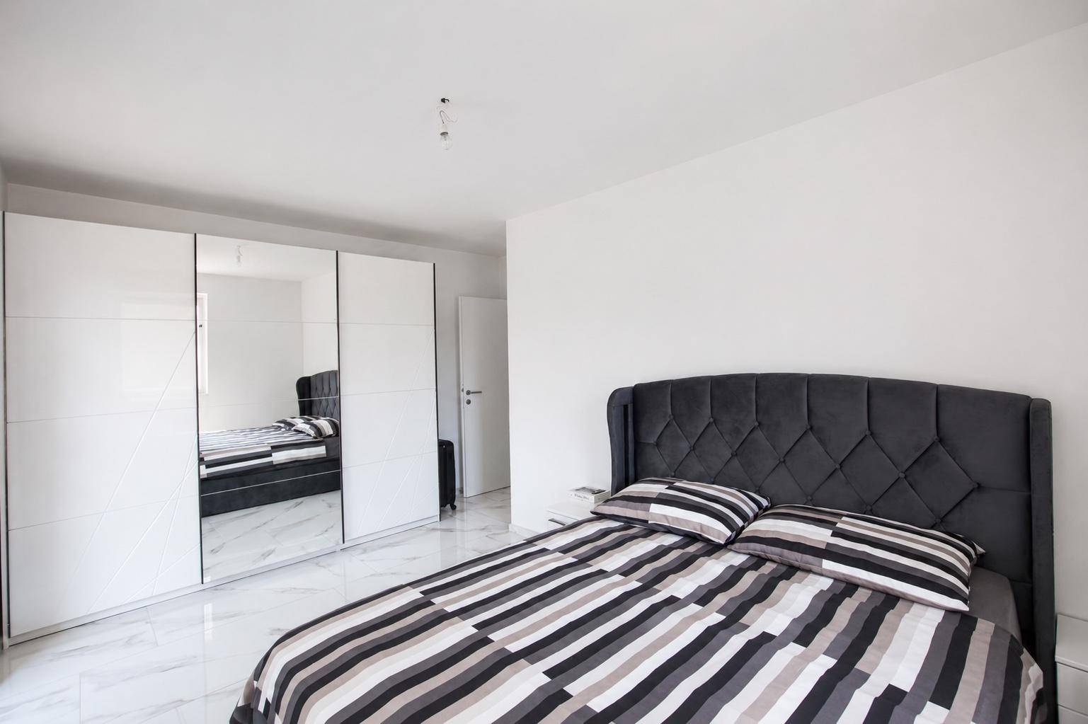 Schlafzimmer mit großem Bett, Spiegelschränken und modernem Marmorboden.