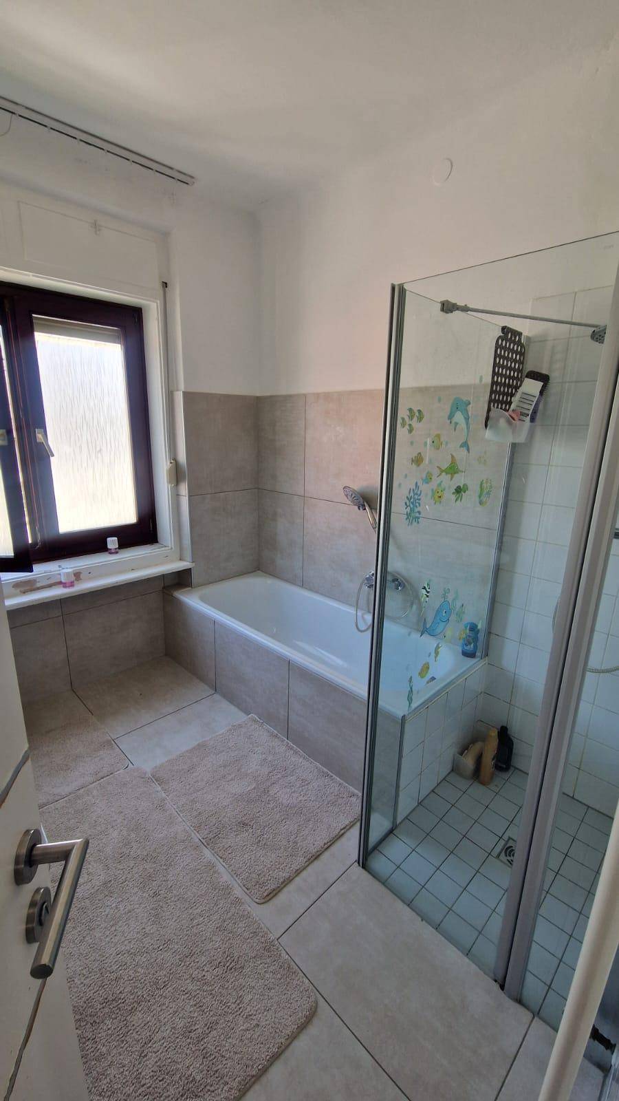Geräumiges Badezimmer mit Badewanne, Duschbereich und Fenster, hell und funktional gestaltet.