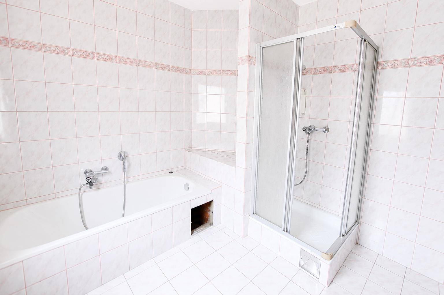 Badezimmer mit weiß gefliesten Wänden, einer Badewanne und einer Duschkabine.