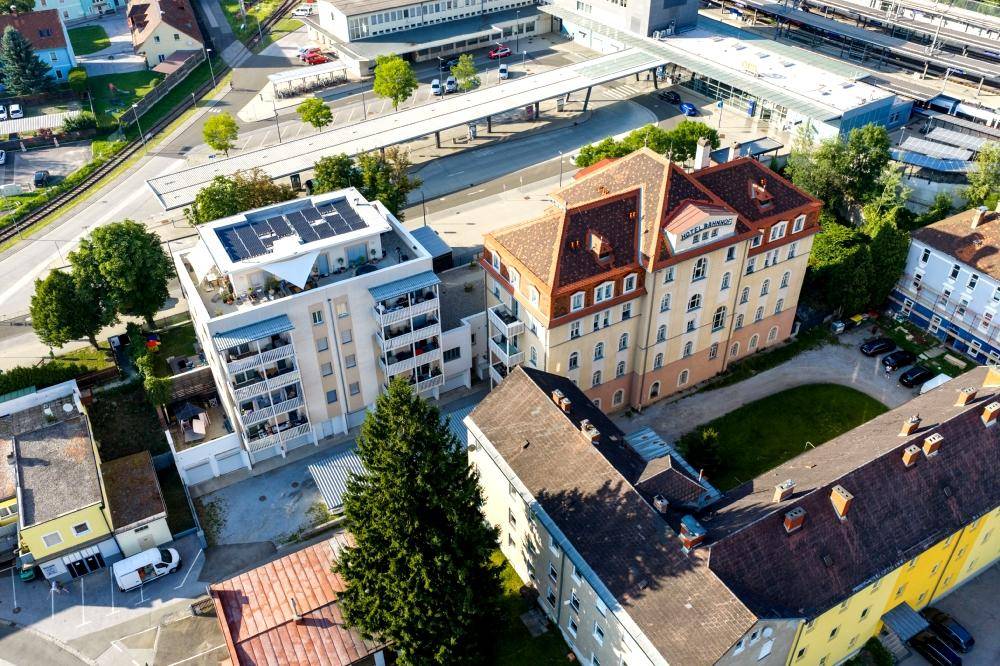 Luftaufnahme von zwei Gebäuden, einem historischen Hotel und einem modernen Wohnhaus mit Solaranlage.