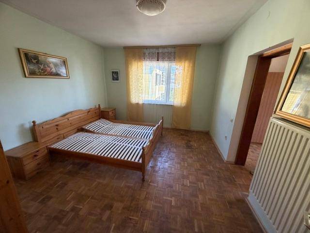 Schlafzimmer mit zwei Einzelbetten, Holzparkett und einem Fenster mit Vorhängen.