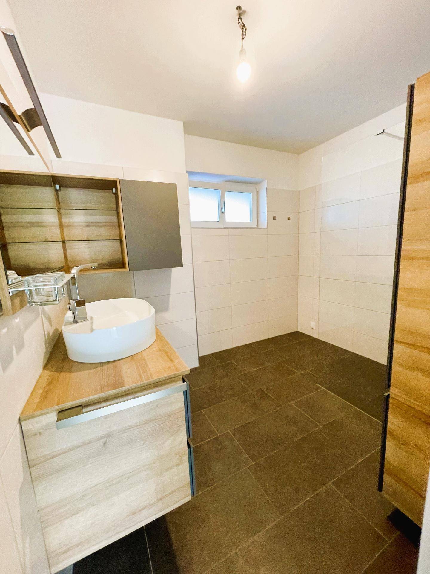 Modernes Badezimmer mit Waschtisch, Spiegel und Fenster, ausgestattet mit dunklen Fliesen.