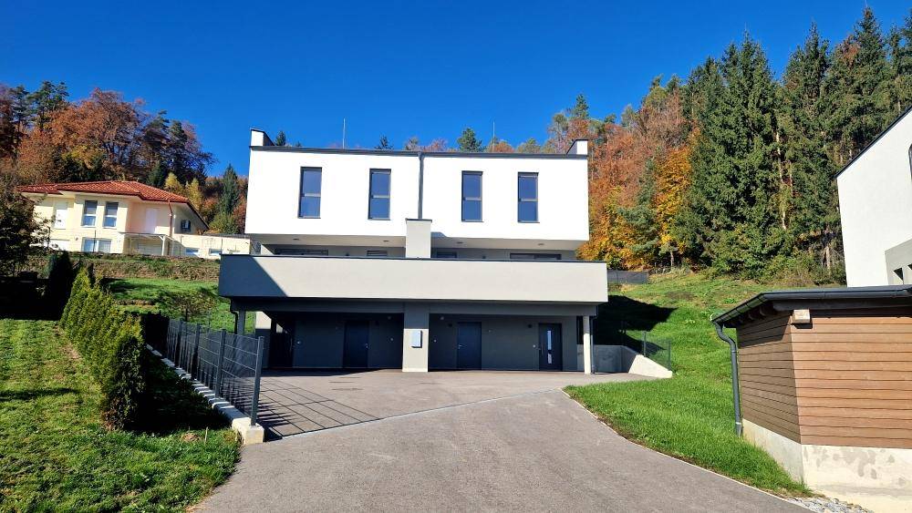 Moderne Doppelhaushälfte mit weißer Fassade und grauen Akzenten, umgeben von grüner Natur.