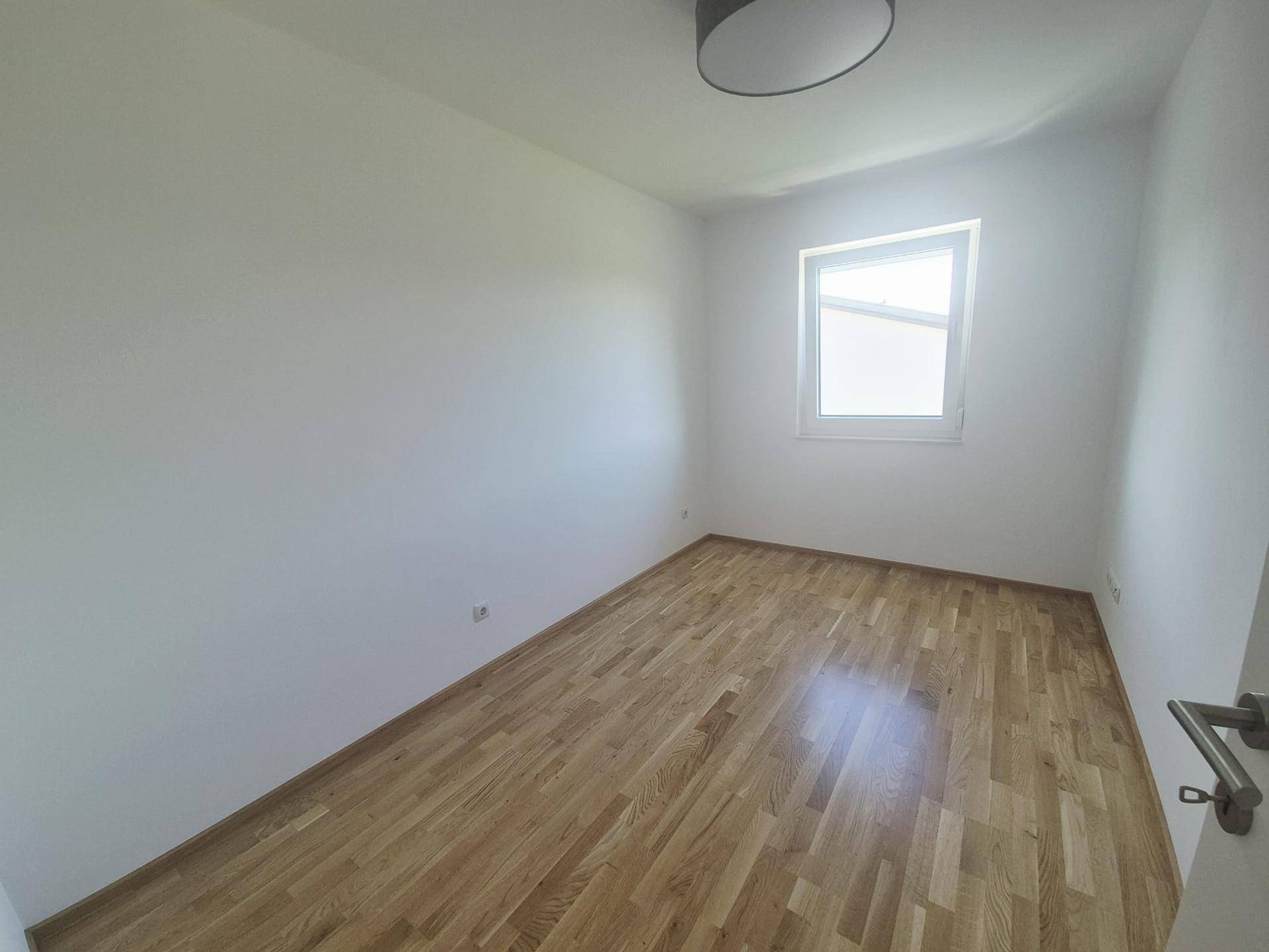 Freundliches Zimmer mit hellem Parkettboden und einem Fenster, das für gute Belichtung sorgt.