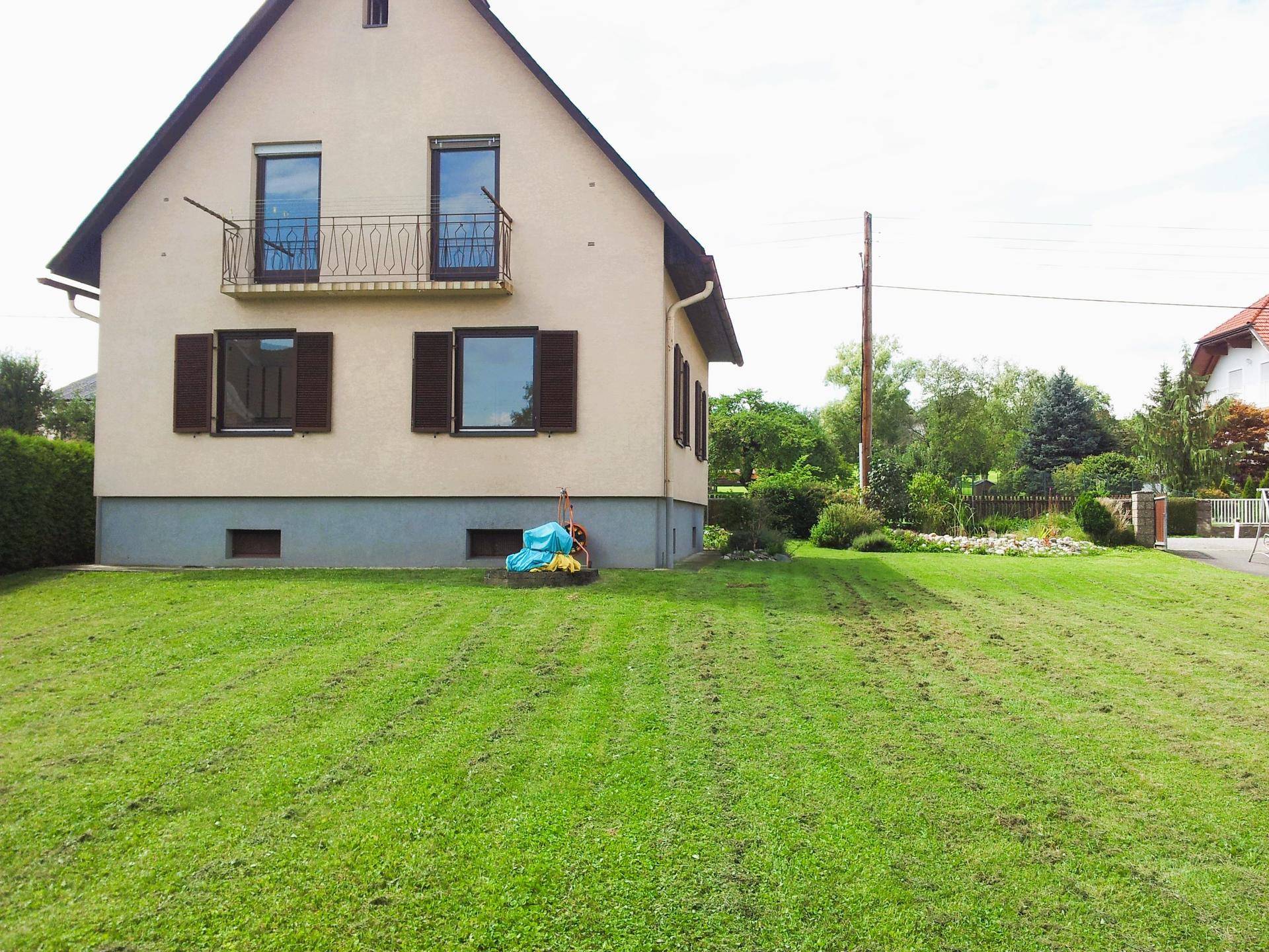 Seitlicher Blick auf das Haus mit gepflegtem Rasen und einem kleinen französischen Balkon im Obergeschoss.