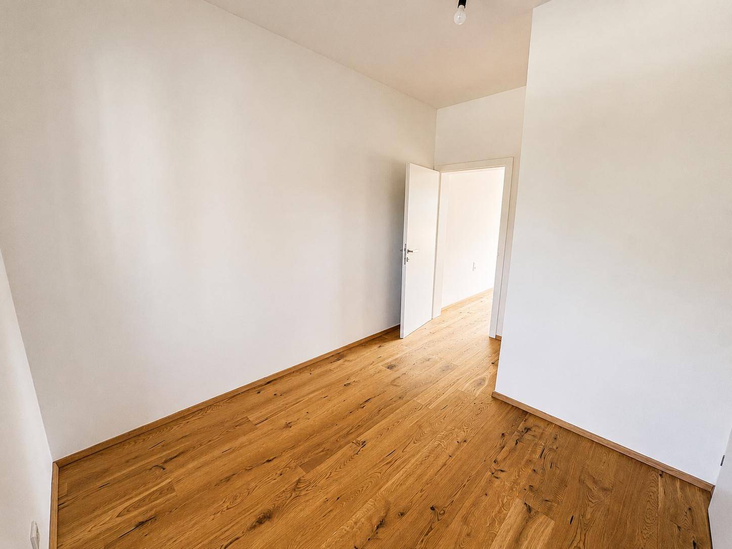 Helles Zimmer mit Holzboden und weiß gestrichenen Wänden, bereit zur individuellen Gestaltung.
