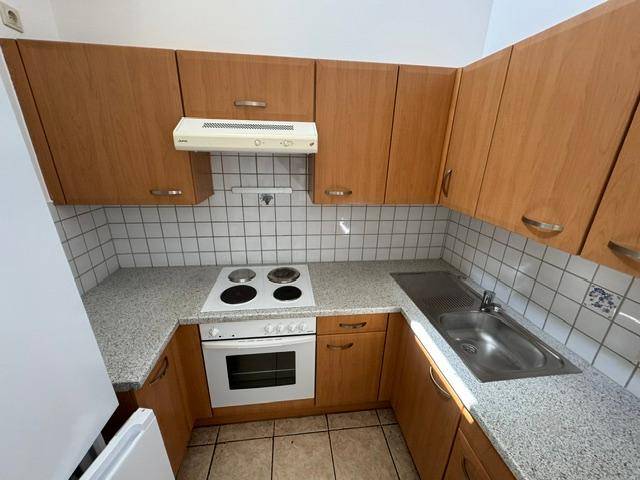 Kleine Küche mit Holzschränken, weißem Fliesenspiegel, Elektroherd und Spüle.