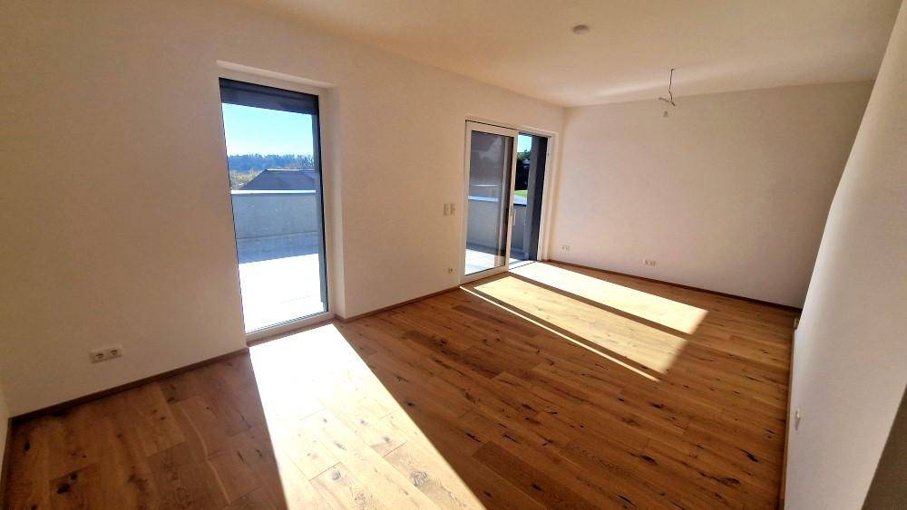 Helles Zimmer mit Holzboden und großen Fenstern, die Zugang zu einem Außenbereich bieten.