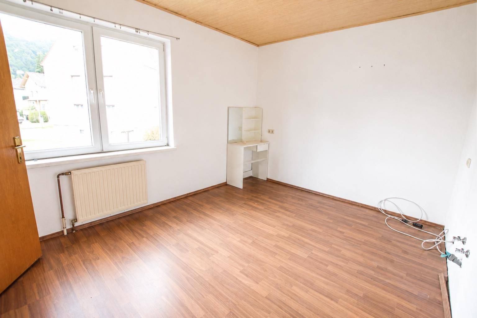 Helles Zimmer mit Laminatboden, Holzdecke und Fensterblick ins Grüne, ideal als Schlafzimmer.