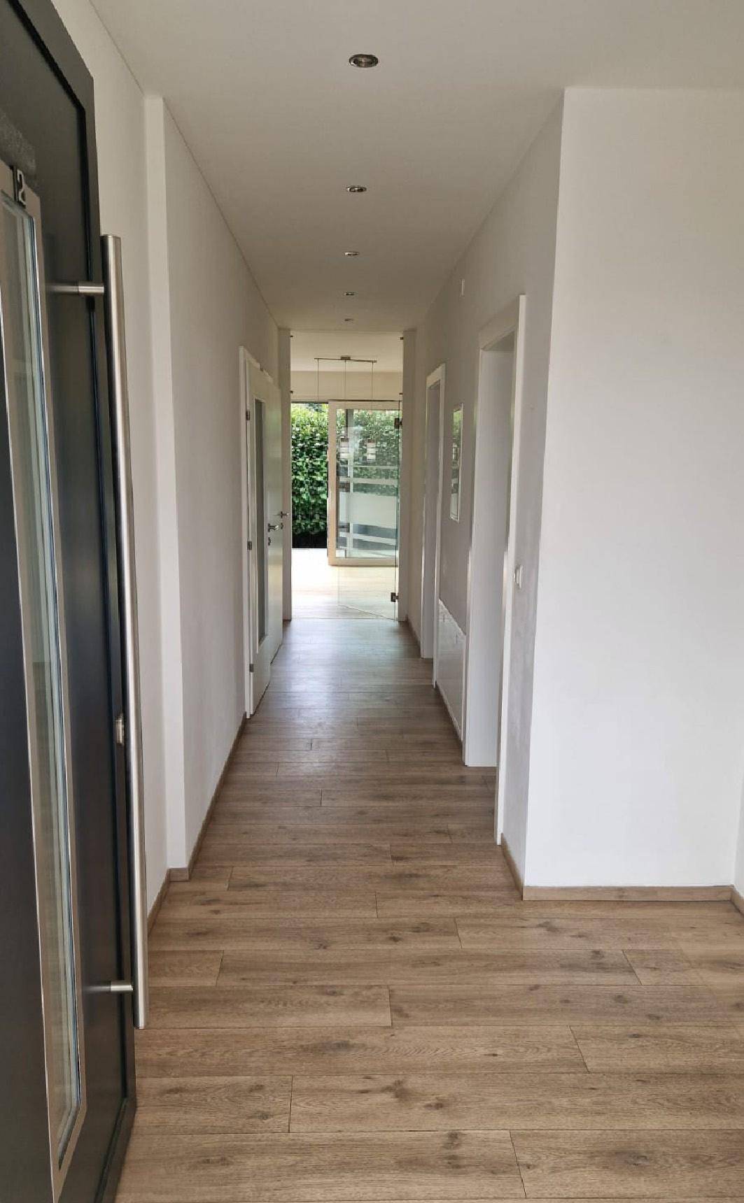 Heller Flur mit Holzparkettboden und Blick durch die Glastür ins Grüne.