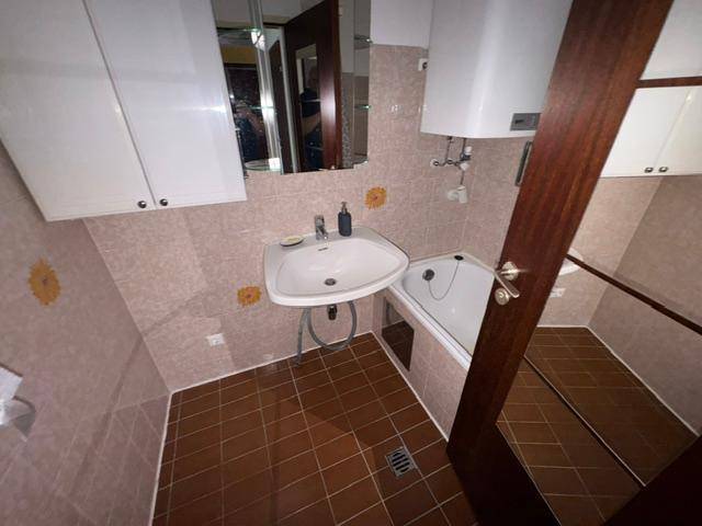Funktionales Badezimmer mit Badewanne, Waschbecken und hellbraunen Fliesen.
