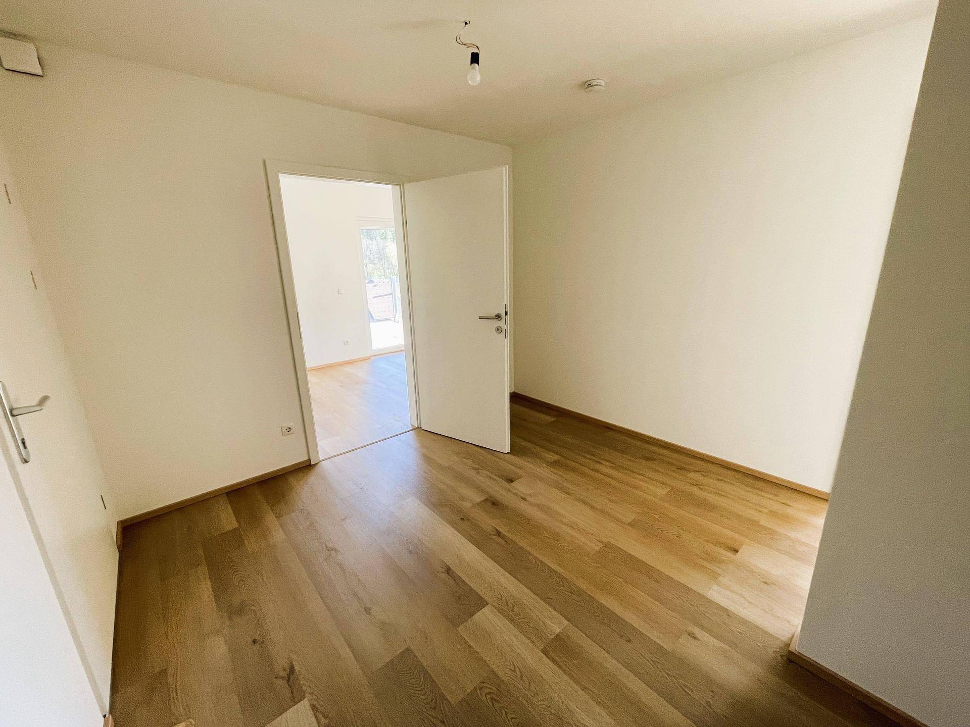 Helles, leeres Zimmer mit neuem Holzboden und weißen Wänden, bereit zum Einzug.