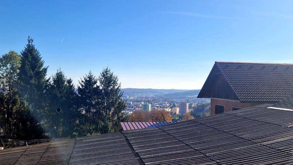 Weiter Blick über eine Stadt oder Ortschaft von einer erhöhten Position mit Dächern im Vordergrund.