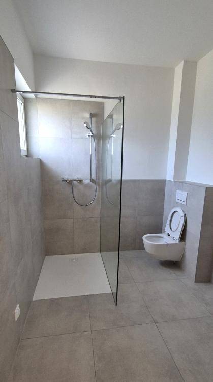 Modernes Badezimmer mit ebenerdiger Dusche, Wand-WC und großen Fliesen.