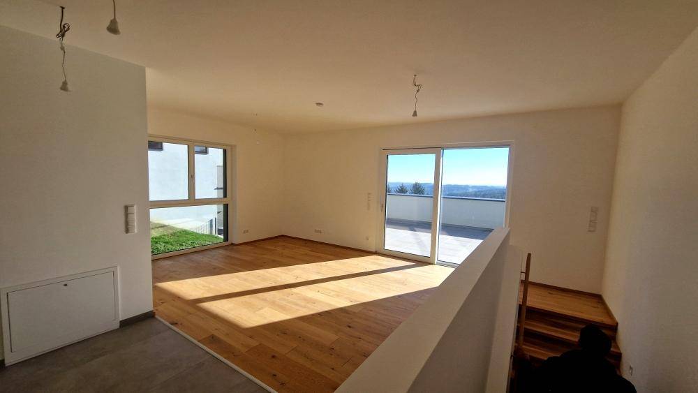 Lichtdurchfluteter Wohnbereich mit Holzboden und Schiebetüren zur Dachterrasse mit Weitblick.
