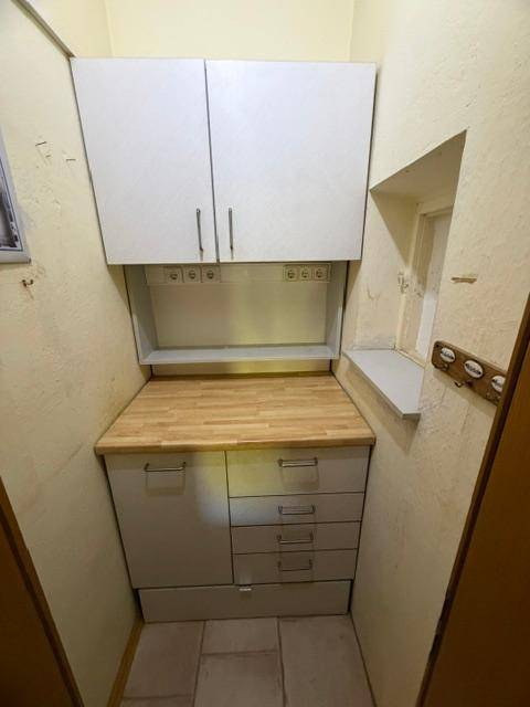 Kleine Küchenzeile mit Holz-Arbeitsplatte und weißen Hängeschränken in einem schmalen Raum.