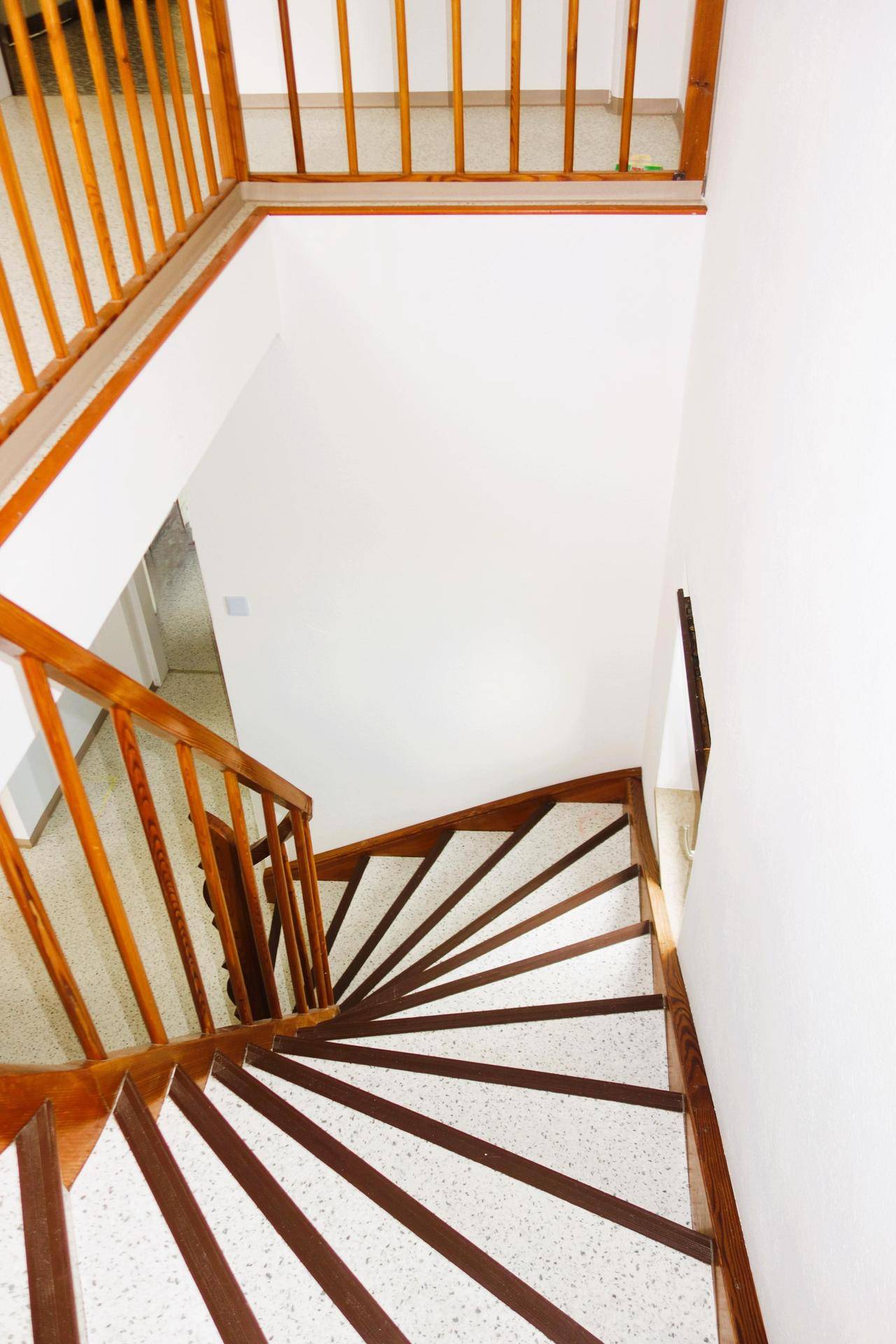 Blick von oben auf die geschwungene Holztreppe mit hellen Stufen und Holzgeländer.