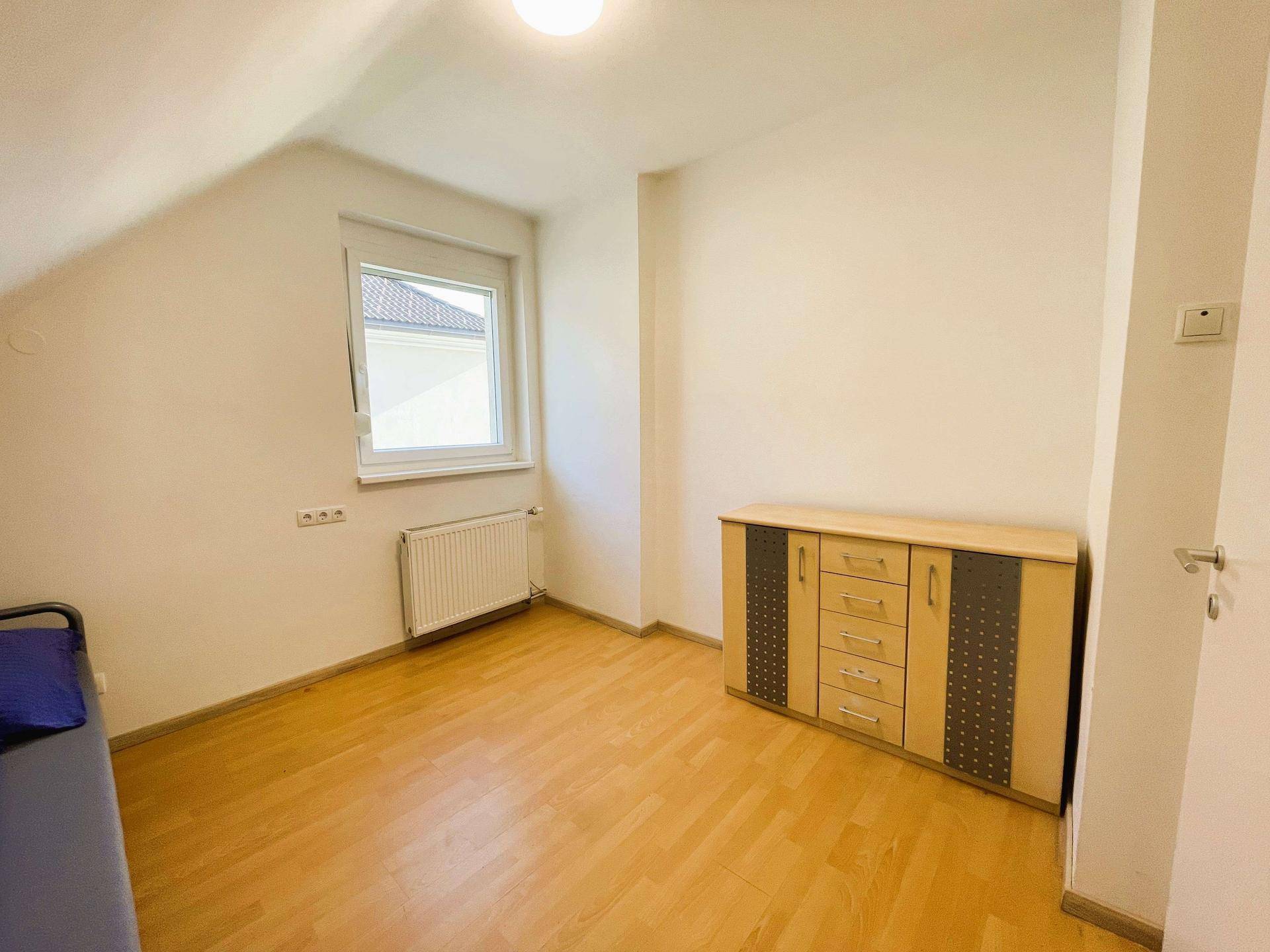 Helles Schlafzimmer mit Holzparkettboden, Heizkörper und Dachschräge.