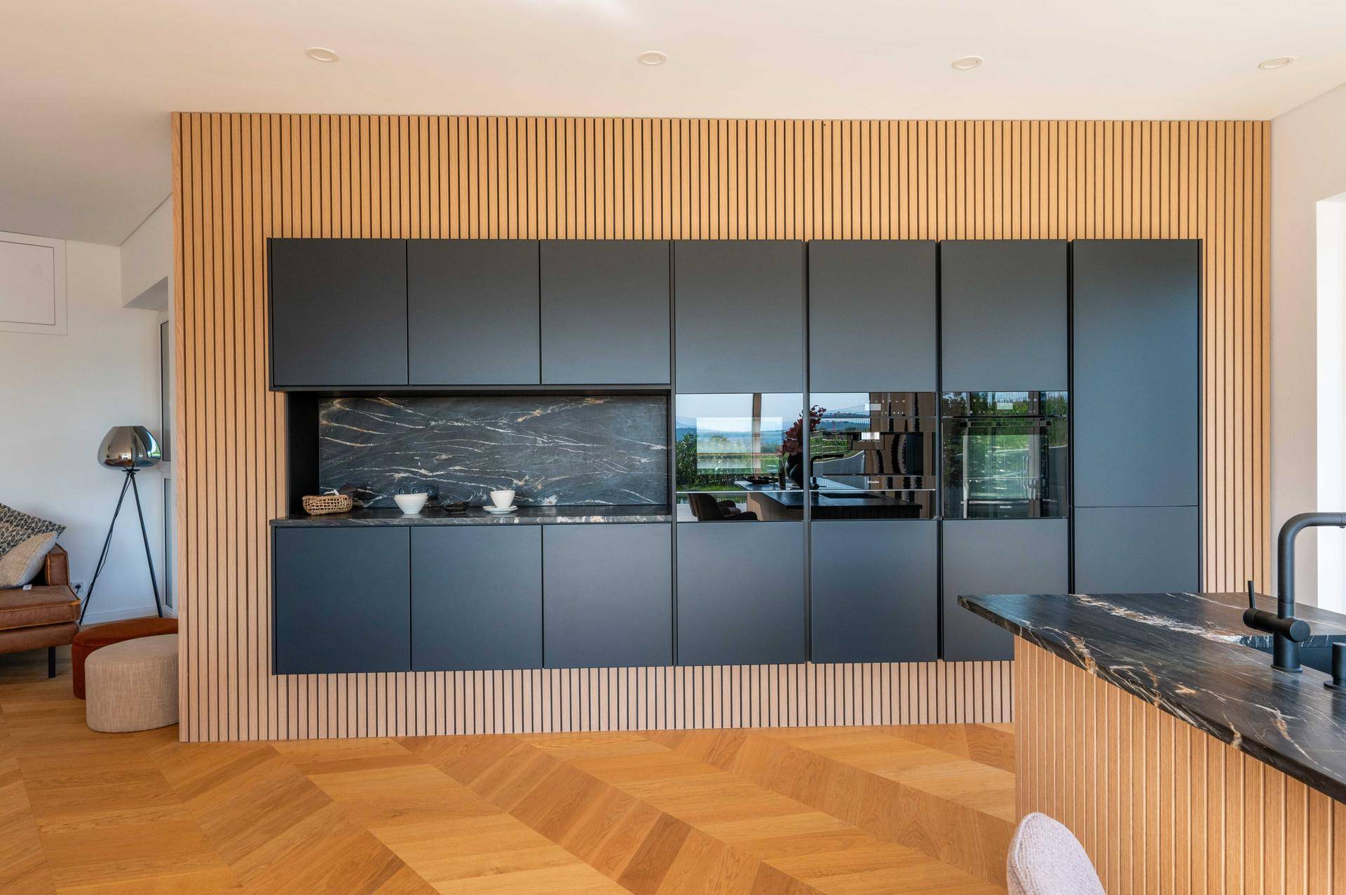 Elegante schwarze Einbauküche mit Marmorarbeitsplatte und Holzlamellenwand.