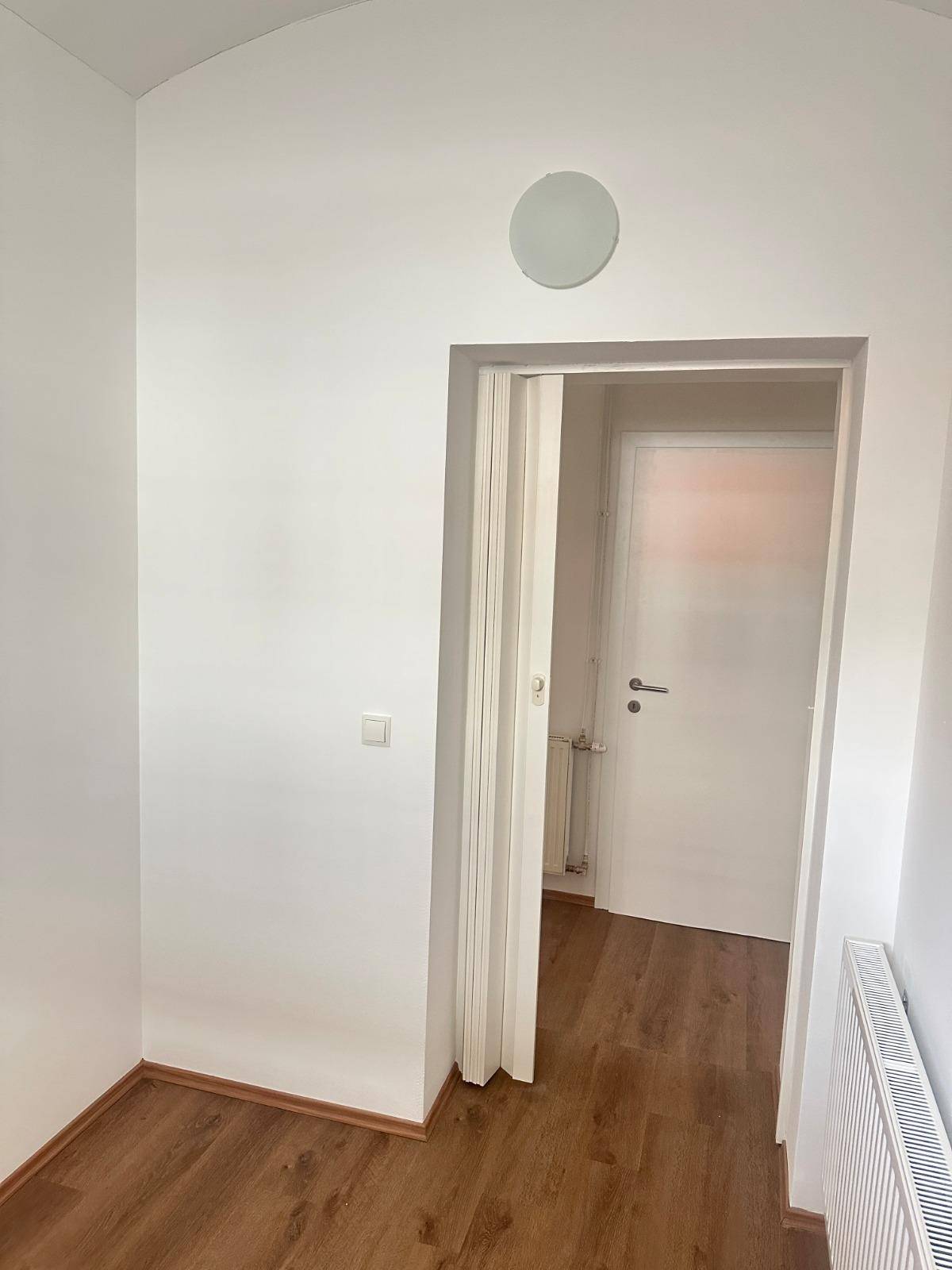 Heller Flur mit Laminatboden und einer Falttür, die zu einem weiteren Raum führt.