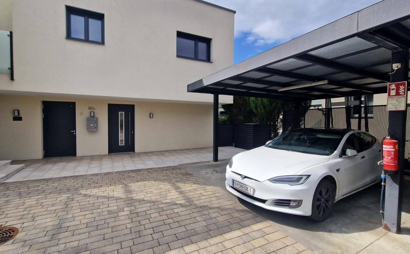Moderne Gebäudefassade mit Eingangsbereich und überdachtem Carport für Fahrzeuge.