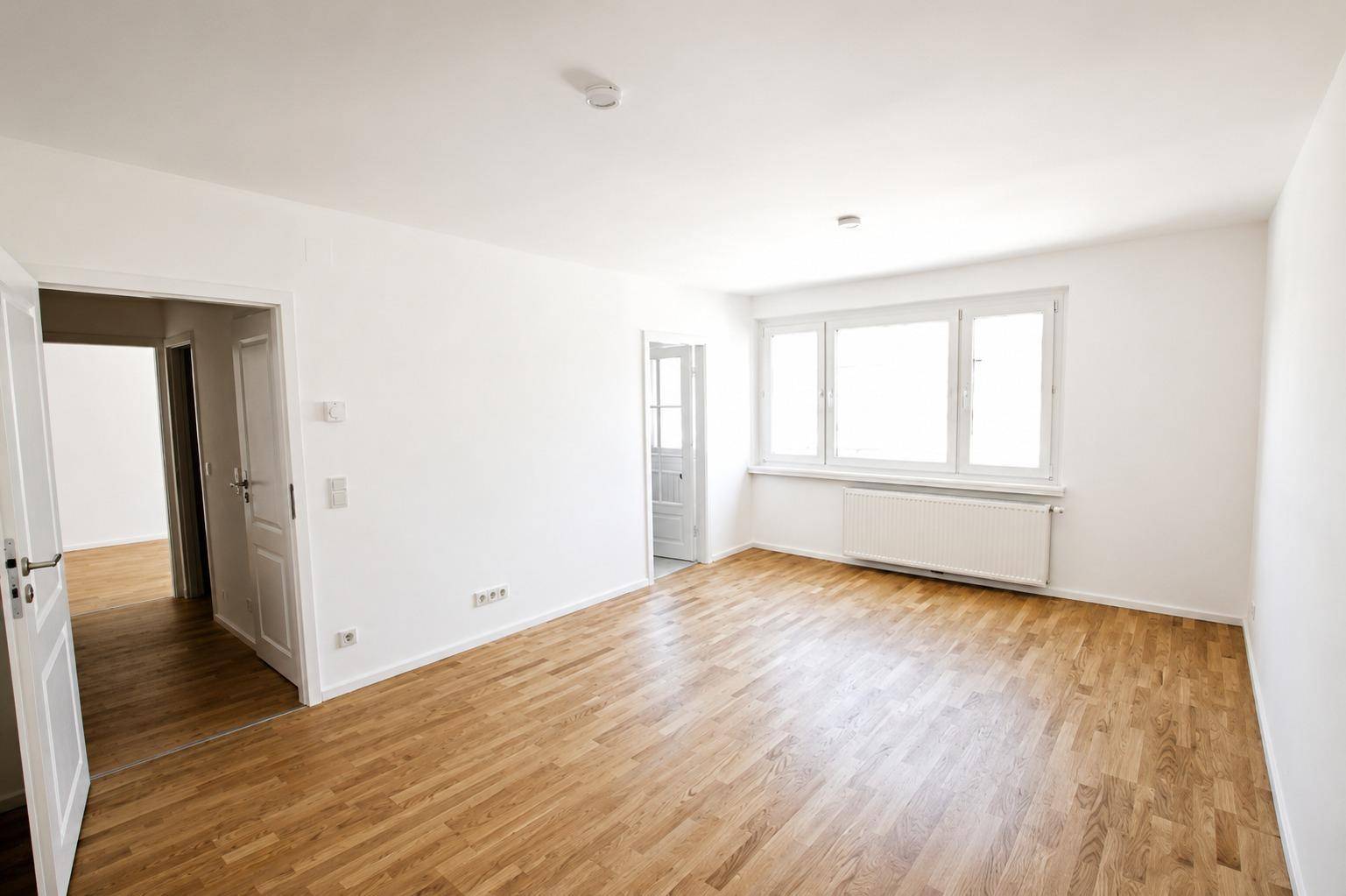 Geräumiges, helles Zimmer mit schönem Parkettboden und großen Fenstern, ideal als Wohnbereich.