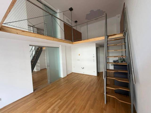 Heller Wohnbereich mit Holzfußboden, einer Galerie und einer modernen Metalltreppe.