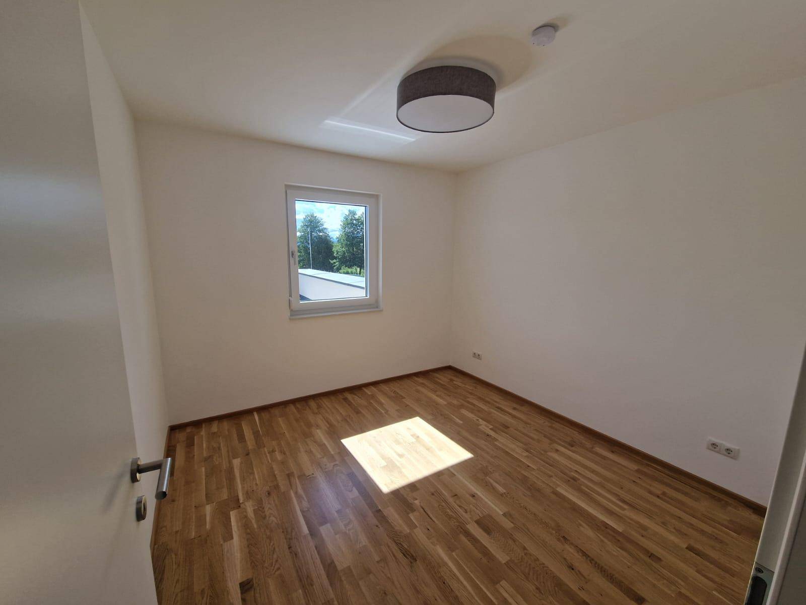 Helles Zimmer mit Eichenparkettboden und einem Fenster, das viel natürliches Licht hereinlässt.