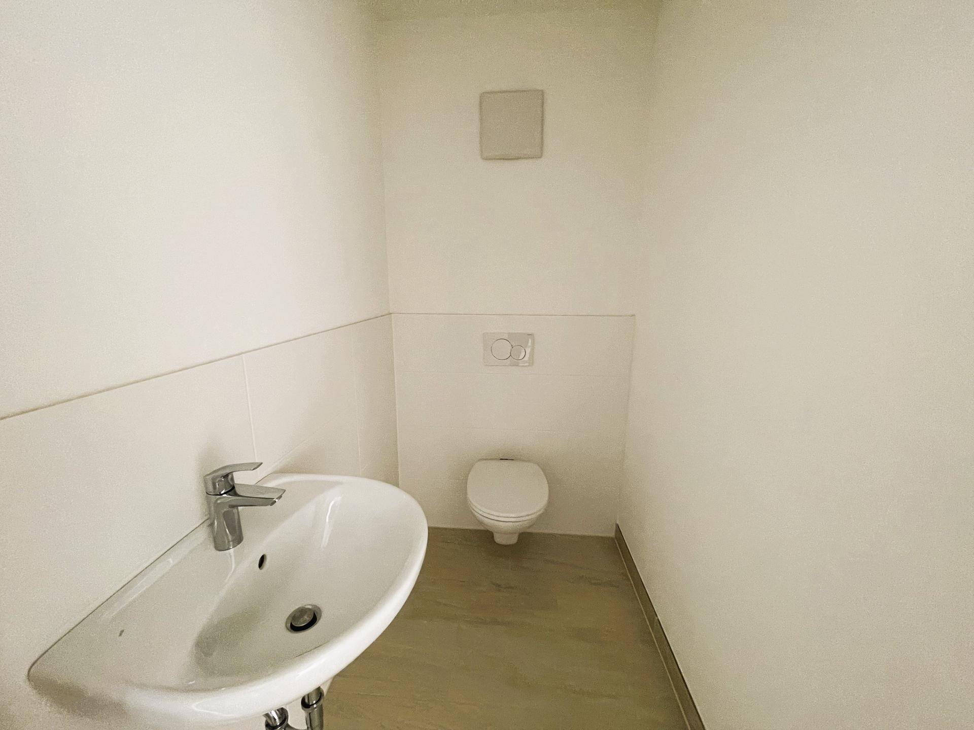 Modernes Gäste-WC mit wandhängender Toilette und kleinem Waschbecken in schlichtem Design.