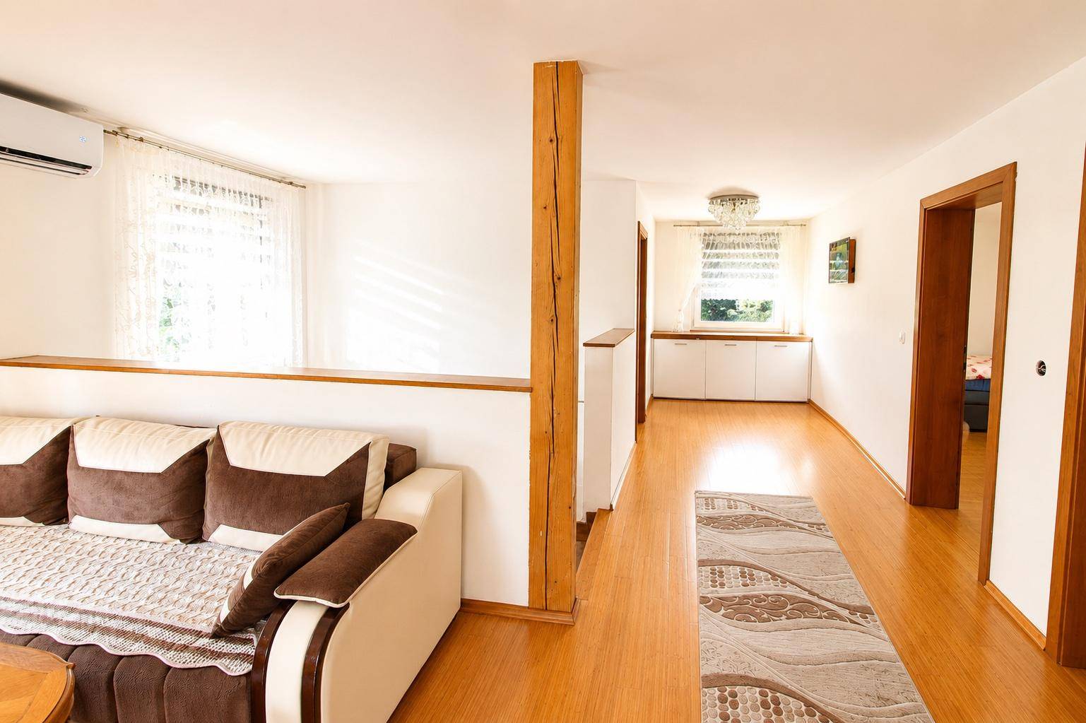 Helles Wohnzimmer mit Sofa, Holzbalken und offenem Übergang zu einem Flur.