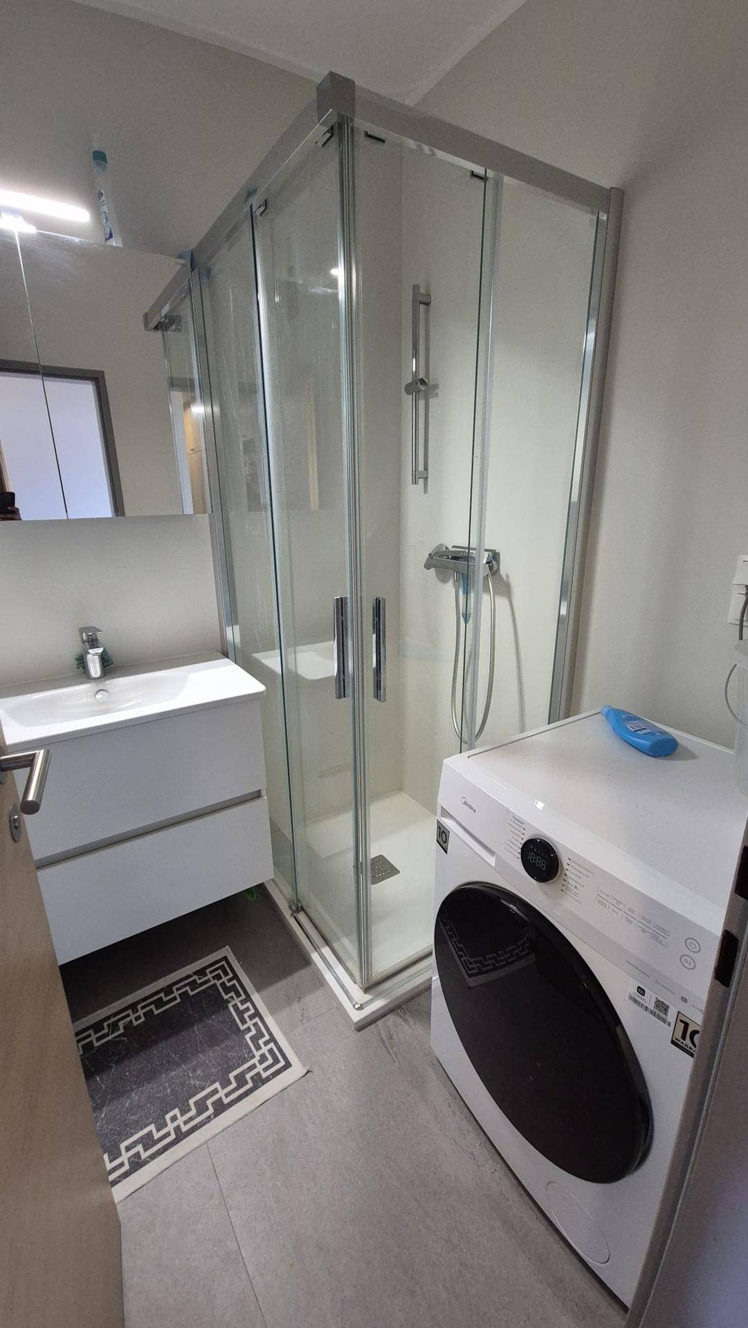 Funktionales Badezimmer mit Duschkabine, Waschbeckenunterschrank und einer Waschmaschine.