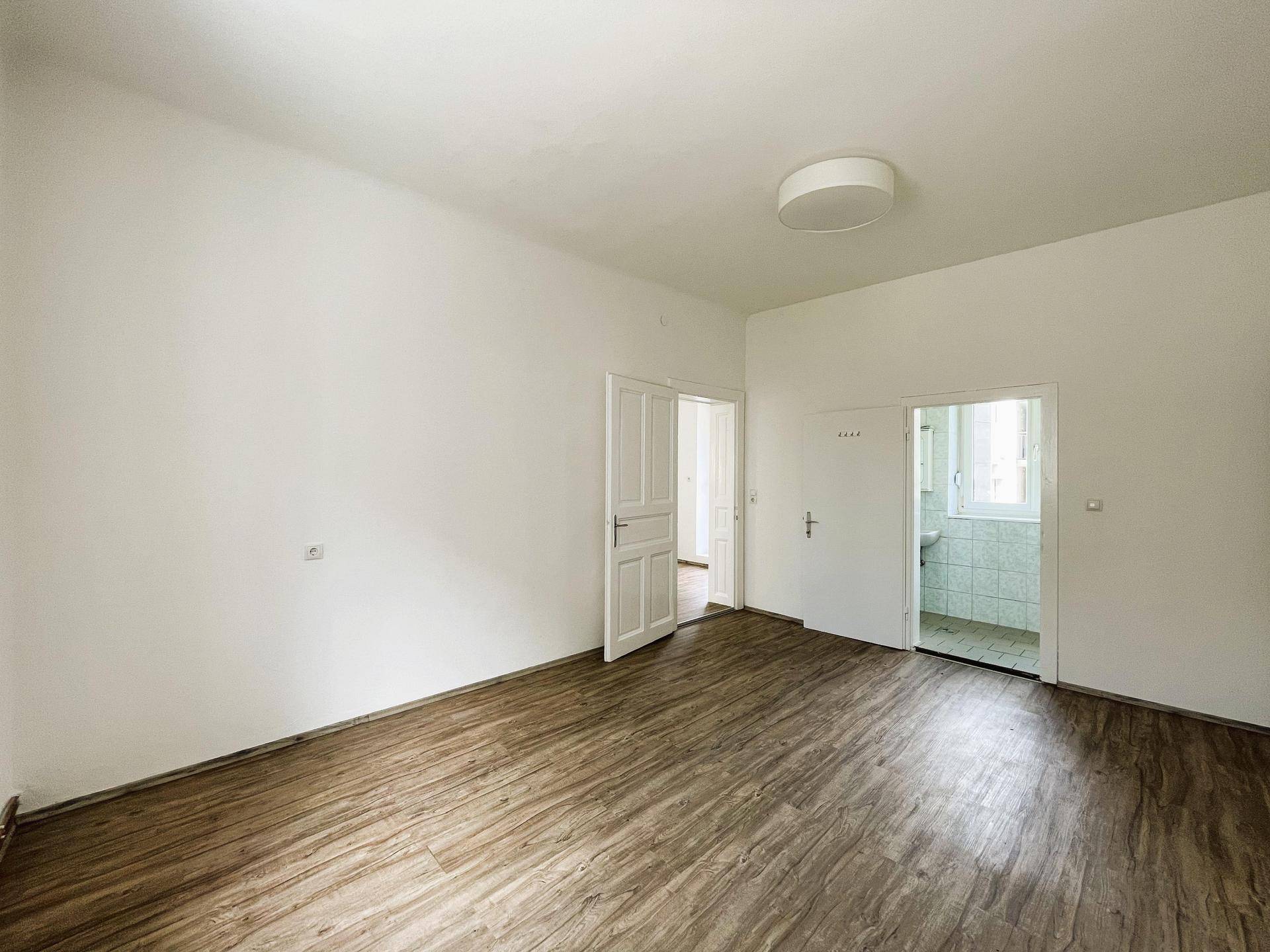 Geräumiges Zimmer mit Laminatboden und zwei Türen, die zu angrenzenden Räumen führen.