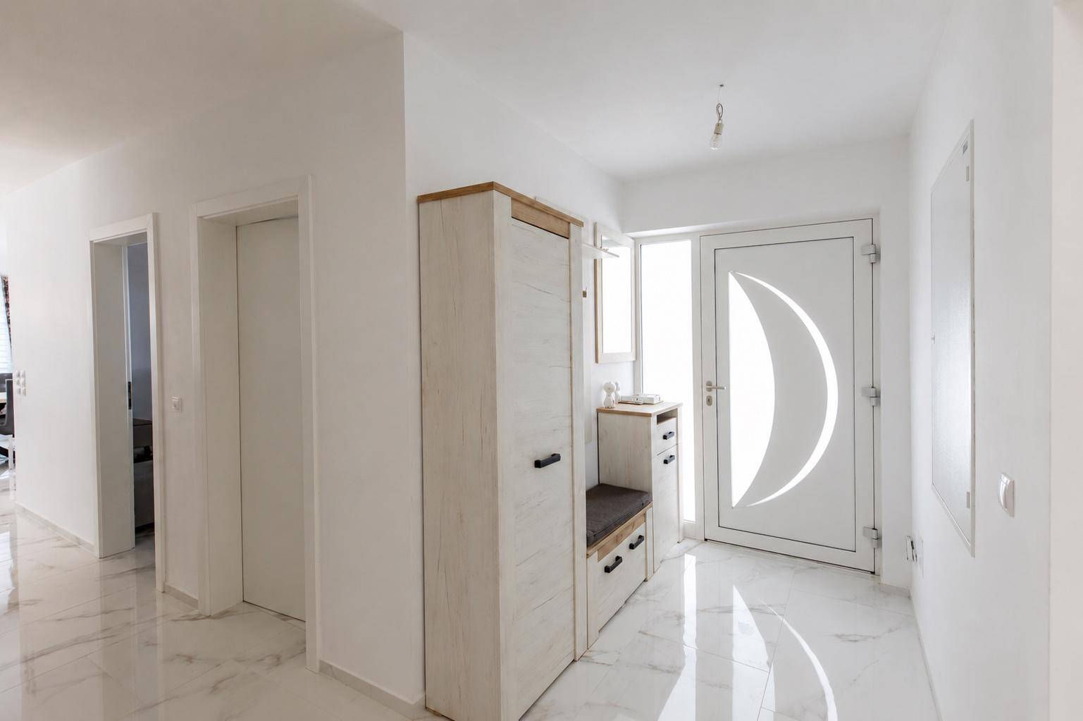 Heller Eingangsbereich mit weißem Marmorboden und moderner Garderobe.