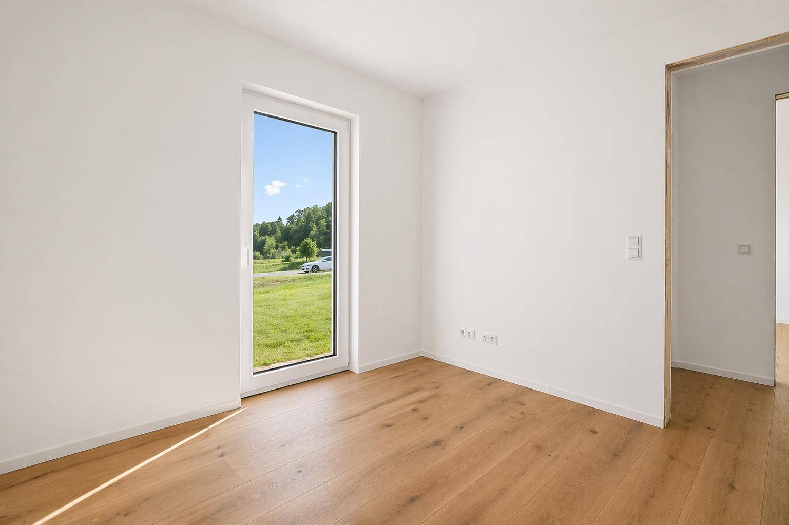 Lichtdurchflutetes Zimmer mit Holzboden und großem Fenster, das einen weiten Blick bietet.