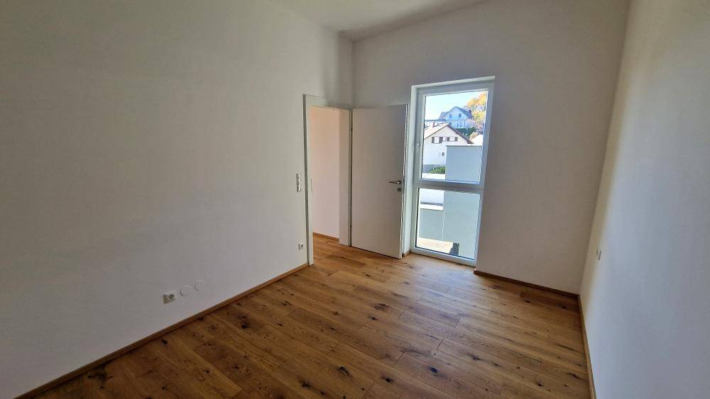 Schlafzimmer mit Holzboden und Fenster, das den Blick nach draußen freigibt.