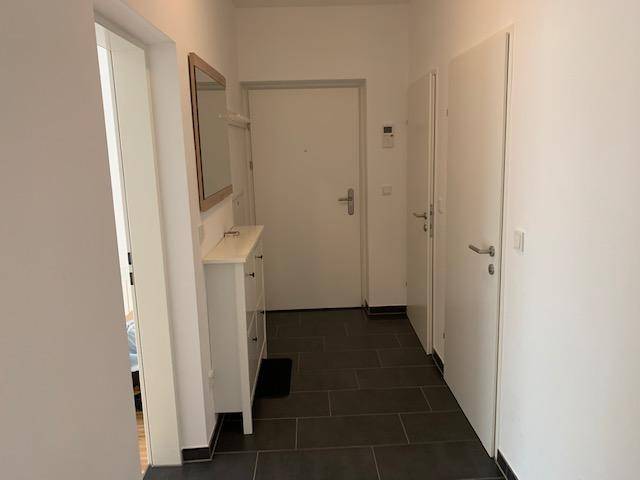 Heller Flur mit dunklen Fliesen, Garderobe und Spiegel, führt zu weiteren Räumen.