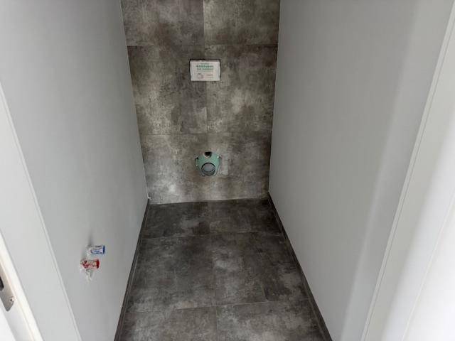 Unfertiger WC-Raum mit grauen Fliesen und Vorbereitung für eine Wandtoilette.