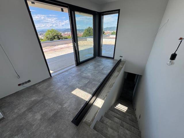 Treppenaufgang zu einer Dachterrasse mit großen Glasfronten und weitem Ausblick.