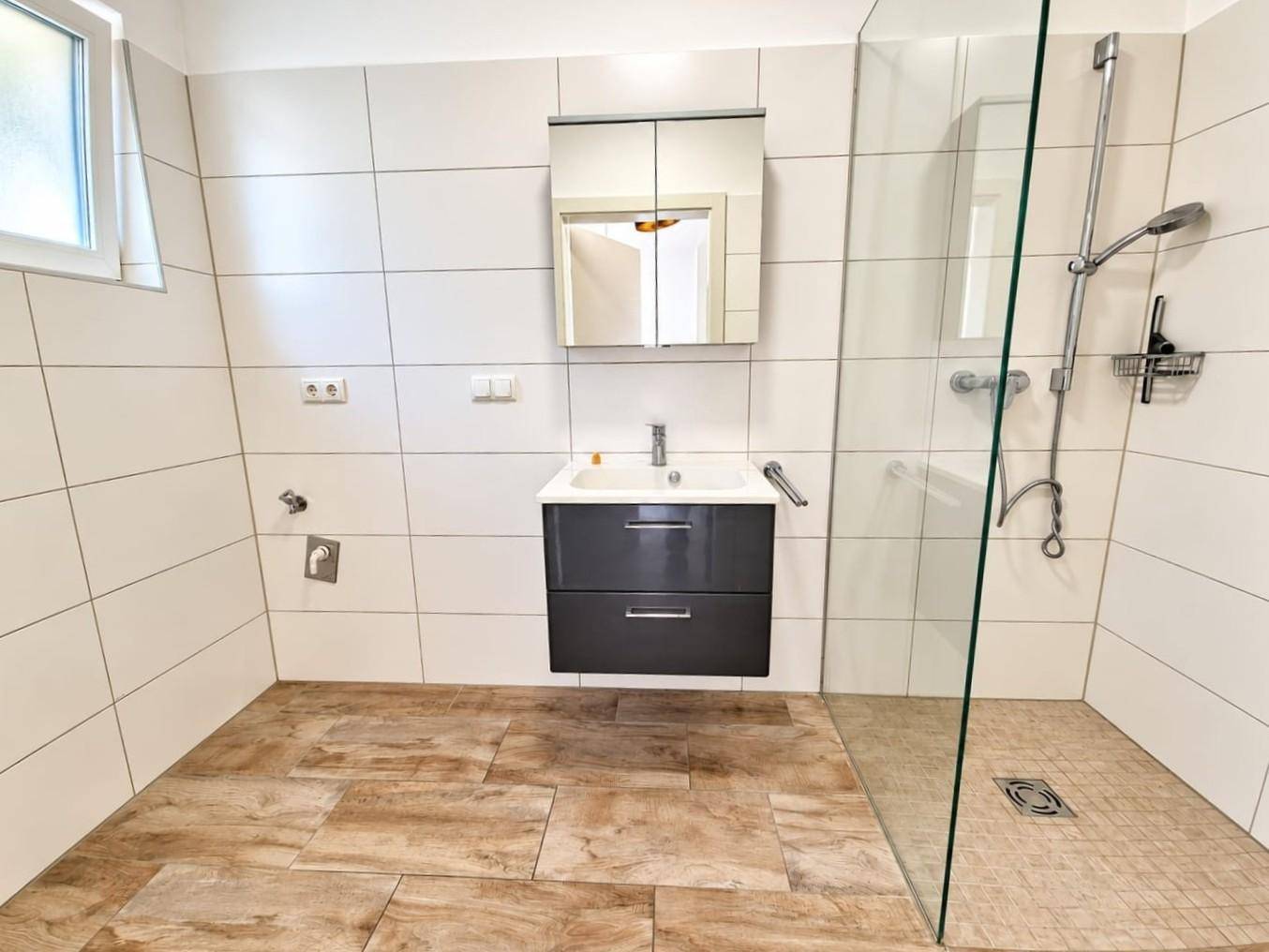 Modernes Badezimmer mit begehbarer Dusche, Waschbecken und Fenster für natürliche Belüftung.