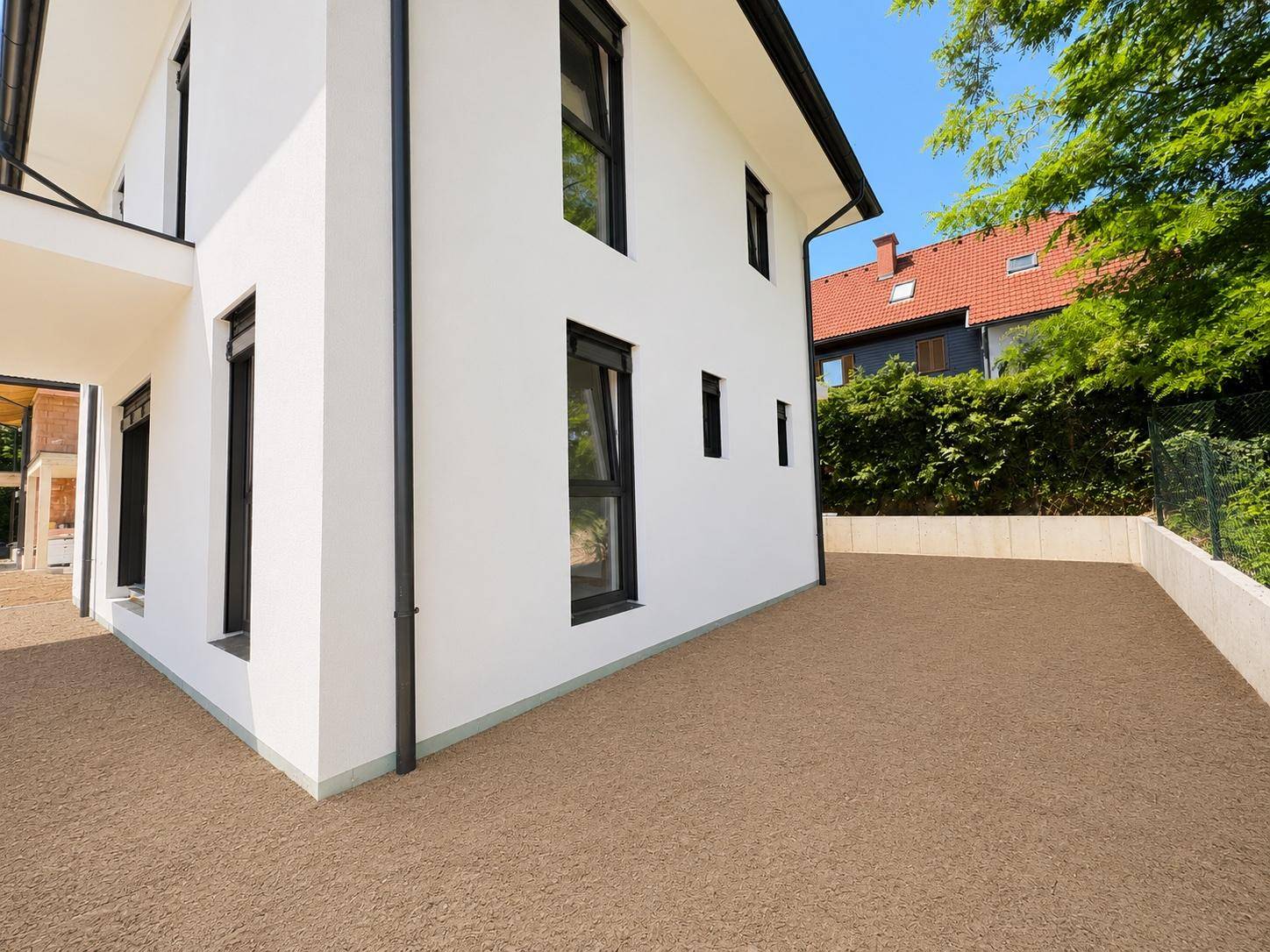 Nahaufnahme der Hausseite mit modernen Fenstern und der umliegenden Kiesfläche.