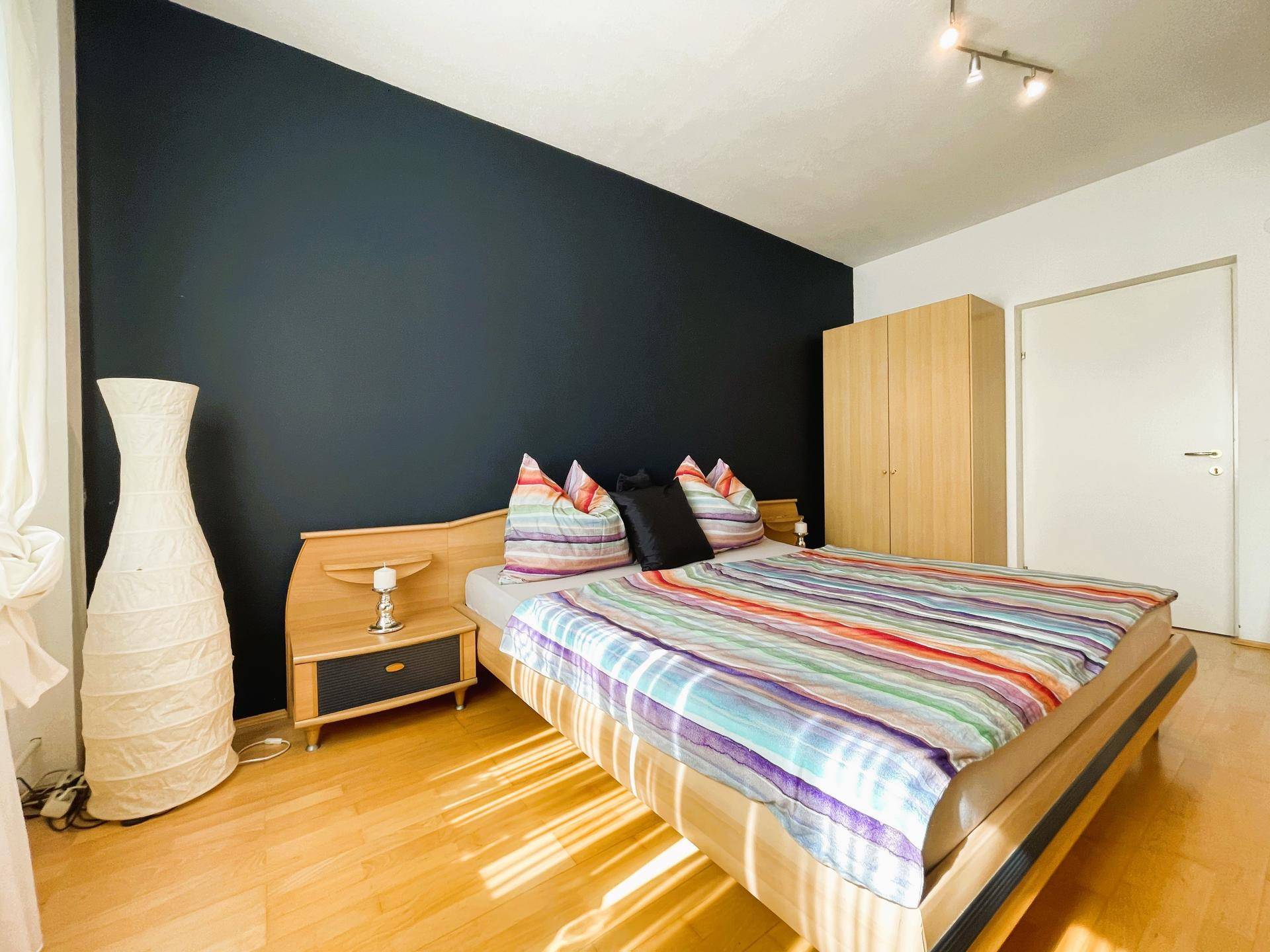Schlafzimmer mit Doppelbett, dunkler Akzentwand und hellem Holzschrank.