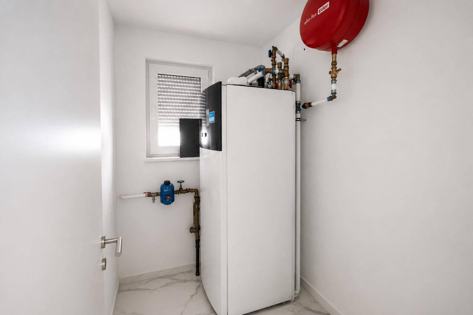 Technikraum mit Wärmepumpe, Warmwasserspeicher und Fenster.