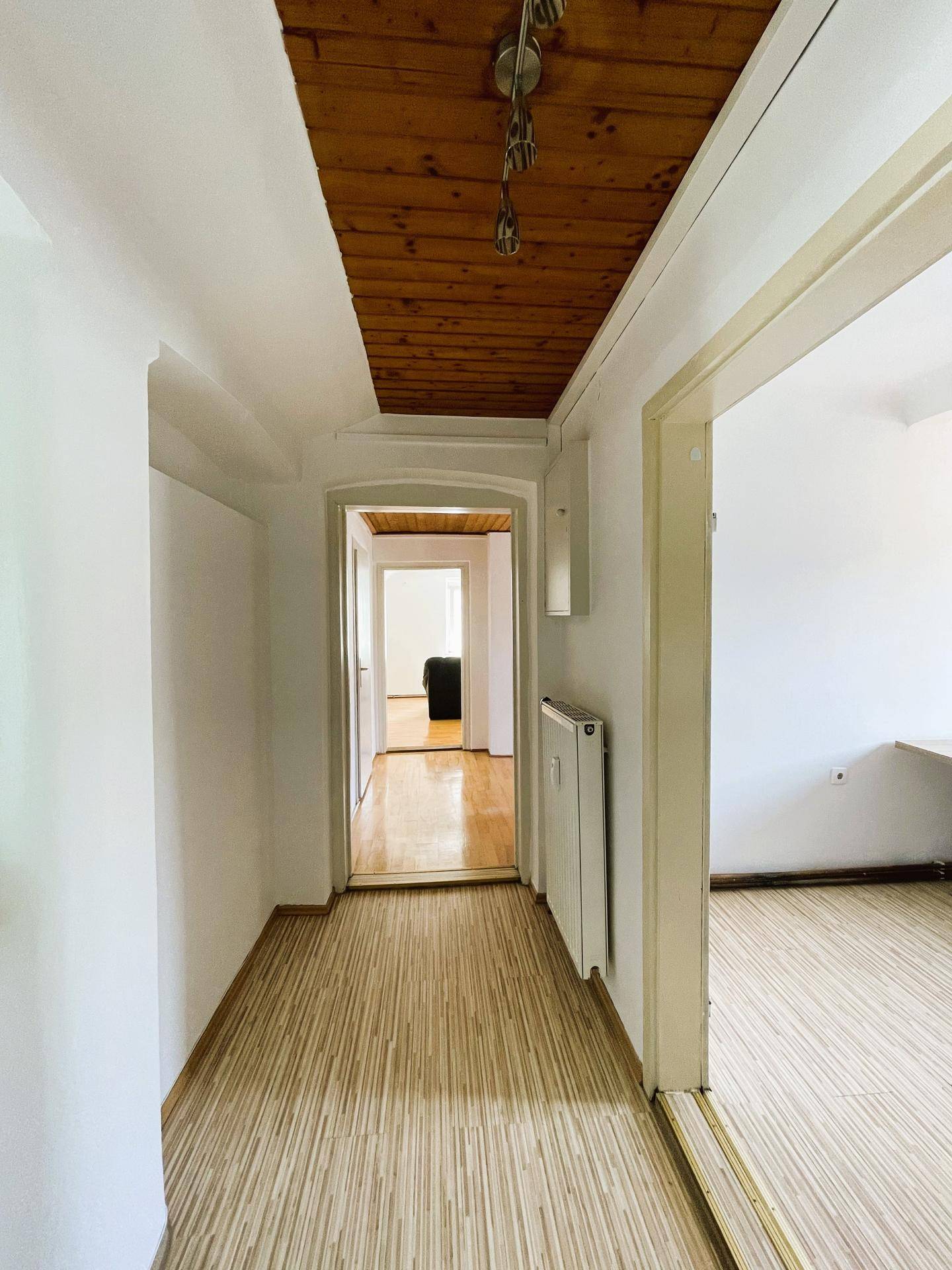 Langer Flur mit Holzdecke und hellem Laminatboden, der zu verschiedenen Räumen führt.