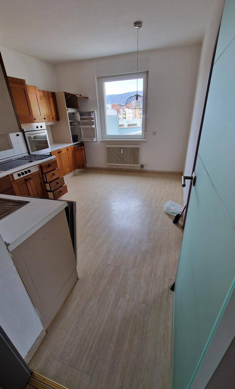 Geräumige Küche mit älteren Holzschränken, Laminatboden und einem Fenster mit Ausblick.