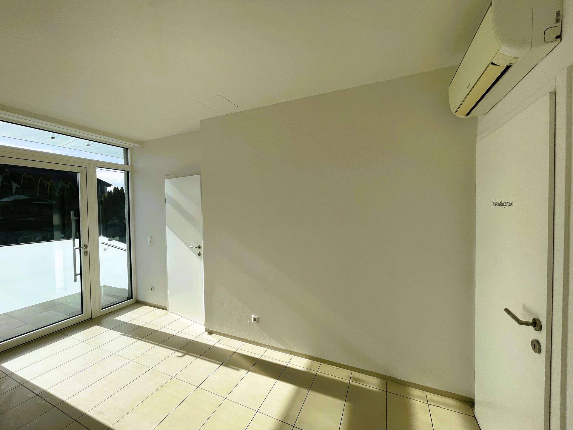 Heller Raum mit Fliesenboden, großen Fenstern und Klimaanlage, ideal für Büro oder Wohnen.